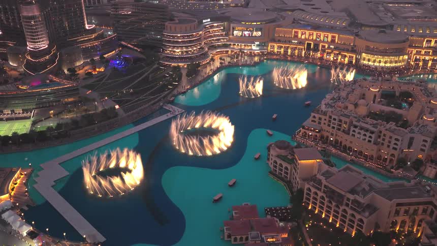 An incredible aerial view of the Dubai Fountain show at night, with illuminated circular water displays surrounded by the glittering city lights