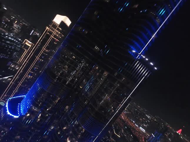 A dizzying aerial shot pans up the side of the illuminated Burj Khalifa at night, ending with a top-down view of the dazzling Dubai cityscape