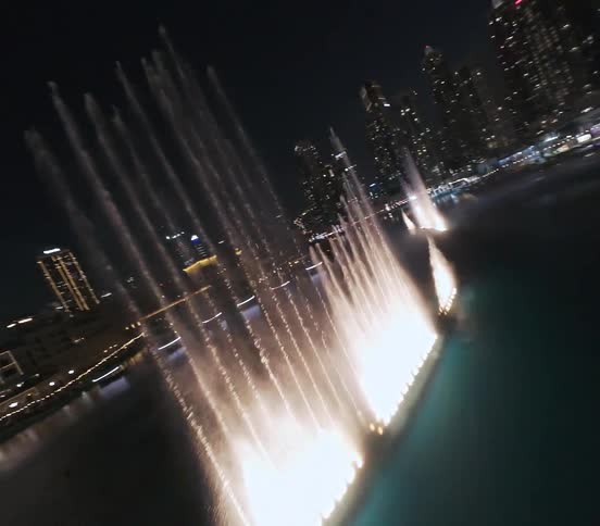 A thrilling FPV drone flight over the spectacular Dubai Fountain show at night, soaring above the illuminated water display against the dazzling city skyline