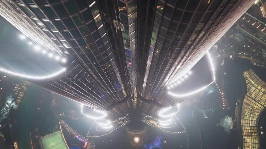An immersive top-down aerial view slowly ascending along the illuminated glass facade of the iconic Burj Khalifa skyscraper at night