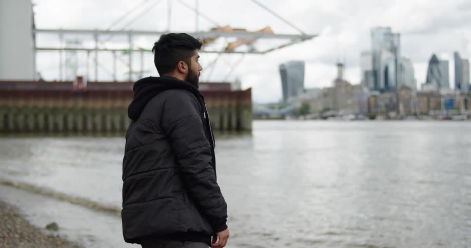 A man skips a stone in super slow motion across the River Thames with the London city skyline in the background