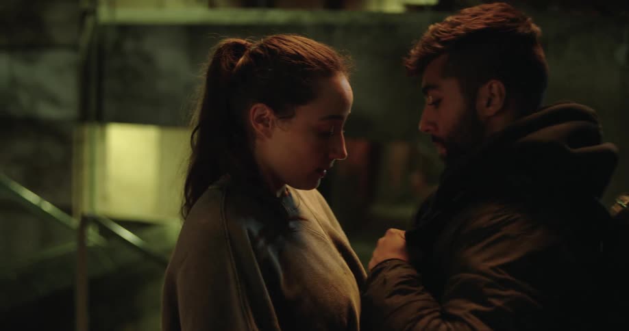 A young delivery driver and his partner share a somber and intimate moment in a gritty underground space at night