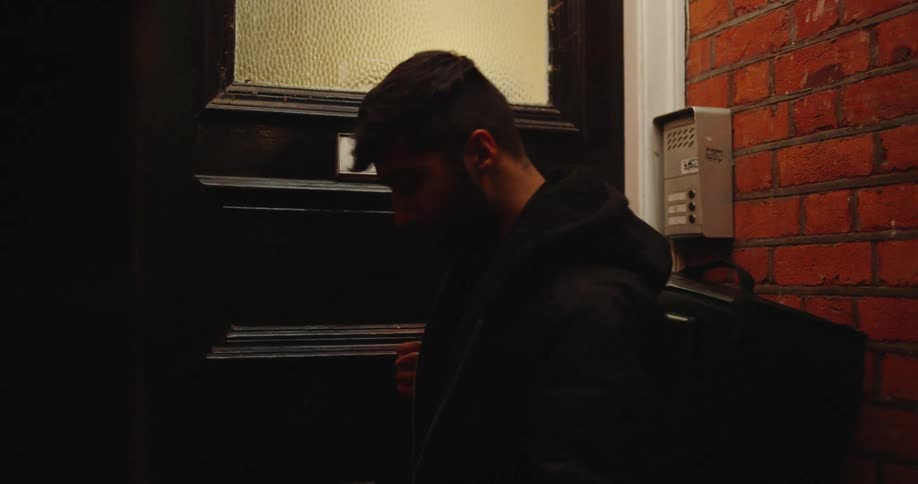 A food delivery driver waits patiently at an apartment door at night before turning to leave