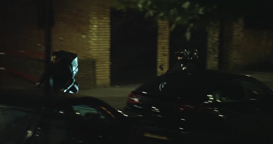 Tracking shot of a food delivery cyclist being followed by two people on a scooter on a dark city street at night