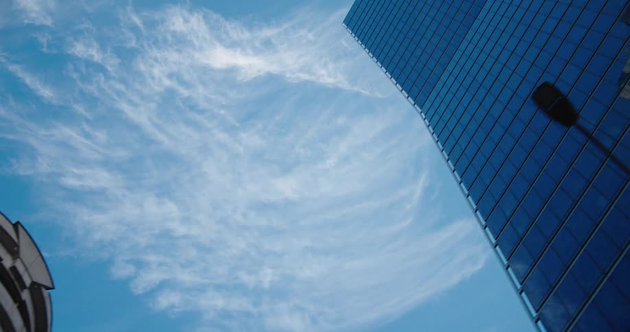 Smooth low-angle pan from a reflective blue glass skyscraper to a classic stone building against a clear blue sky