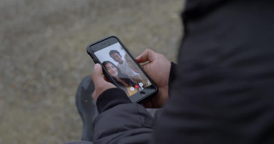 Over the shoulder view of a man having a video call on his smartphone with his family, a woman and young boy