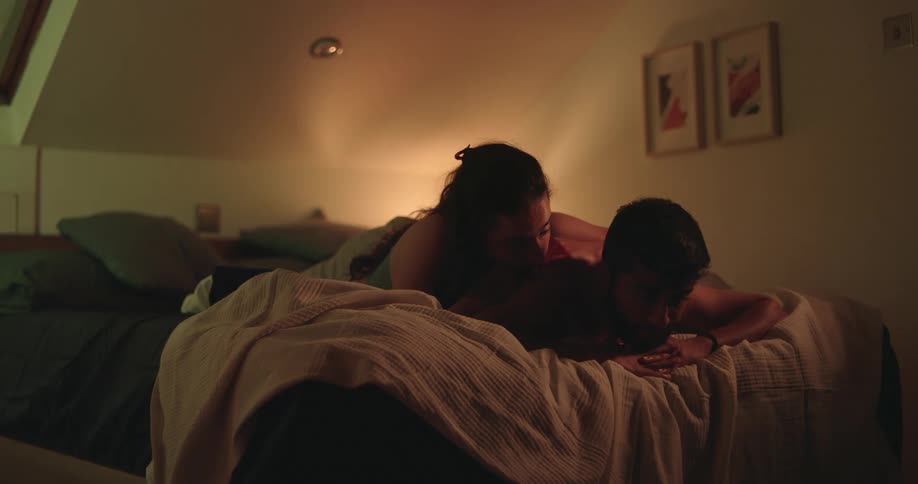 A loving couple embraces intimately in a dimly lit attic bedroom