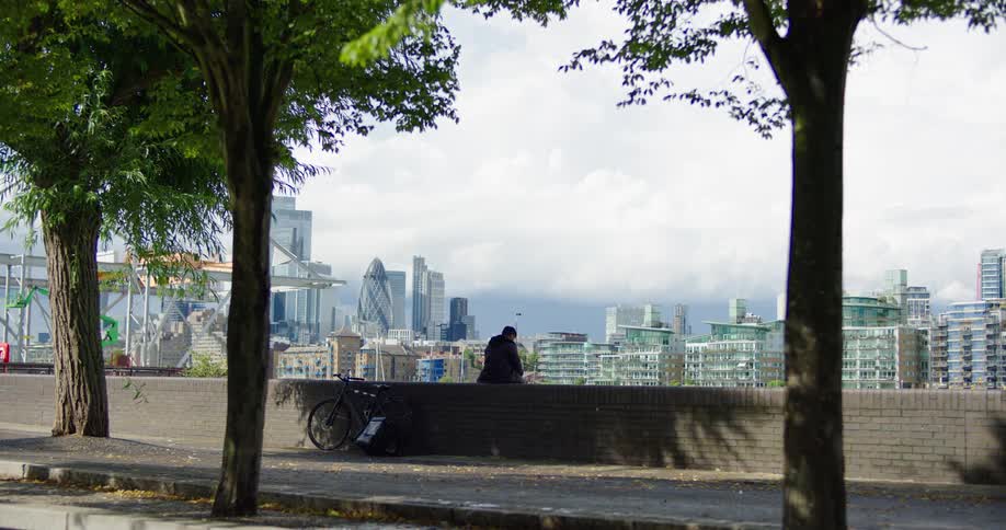 A lone person with a bicycle sits on a wall, peacefully contemplating the iconic London city skyline from a distance