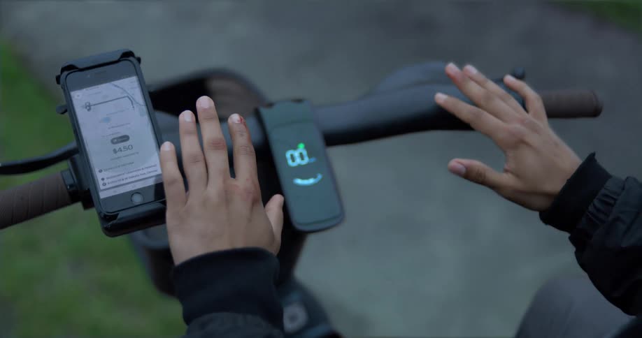 A first-person view of a person with scraped hands sitting on an electric scooter after an accident, with a rideshare app open on a smartphone