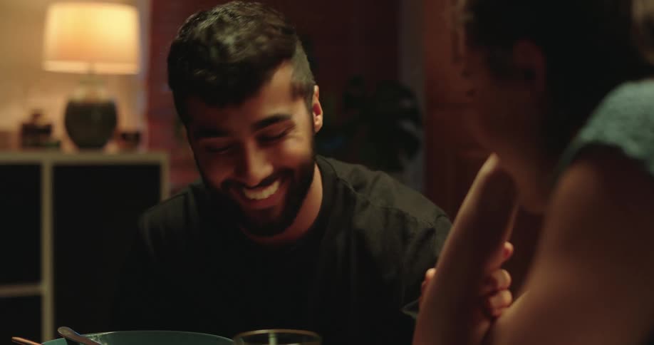 A close-up shot of a young man smiling and engaging in an intimate conversation with his partner during dinner at home