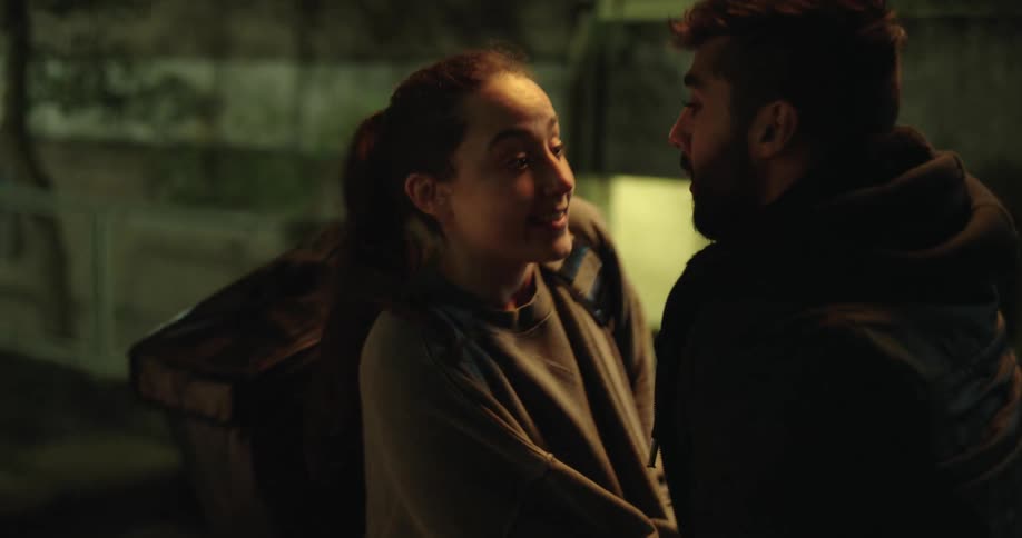A female delivery driver shares a quiet, romantic moment with her boyfriend on urban steps at night