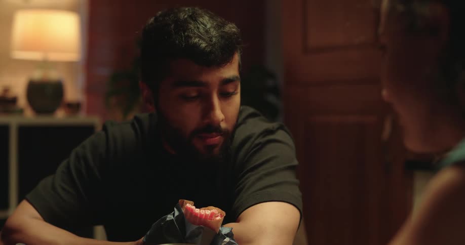 A man smiles as he unwraps a quirky gift of a dental cast from his girlfriend before they share a romantic kiss