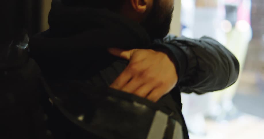 Over-the-shoulder close-up of a delivery driver with his hand in his courier bag while waiting for an order at night