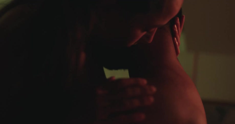 A sensual couple in silhouette kisses and caresses each other in the warm glow of a dimly lit room