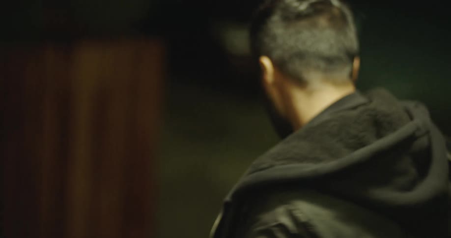 A young, injured food delivery driver with a cut on his face walks slowly down a dark street at night, looking weary and defeated