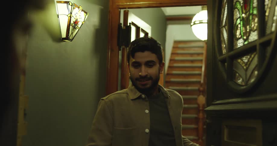 A man opens his front door to a visitor after hearing a knock, looking surprised and then welcoming