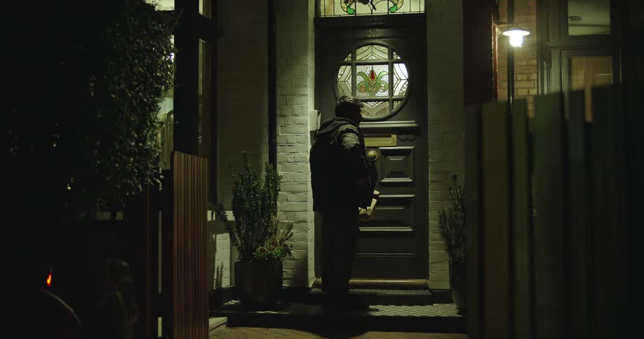 A food delivery courier rides up to a house at night, walks to the door, and hands the order to the customer who answers