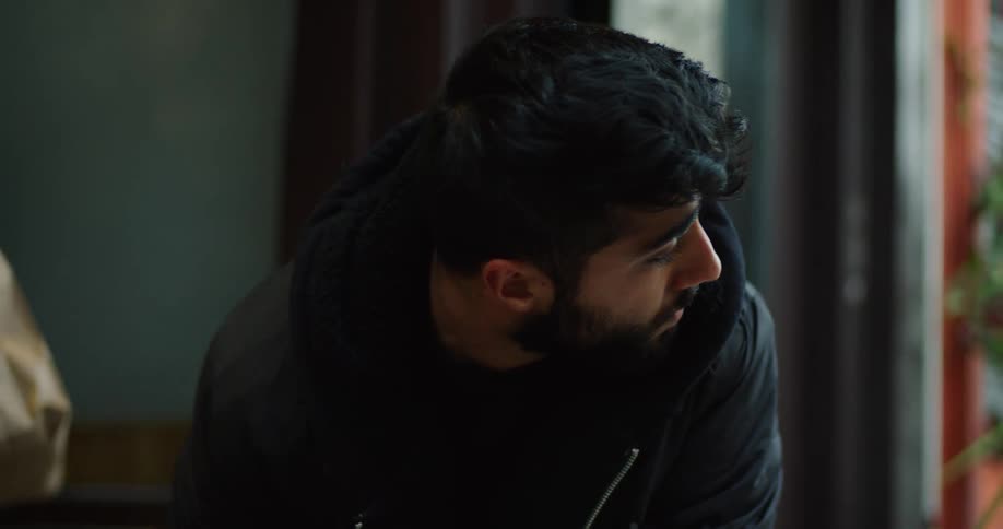 A cautious young man in a black jacket looks around suspiciously before accepting a paper bag and putting it in a large delivery bag