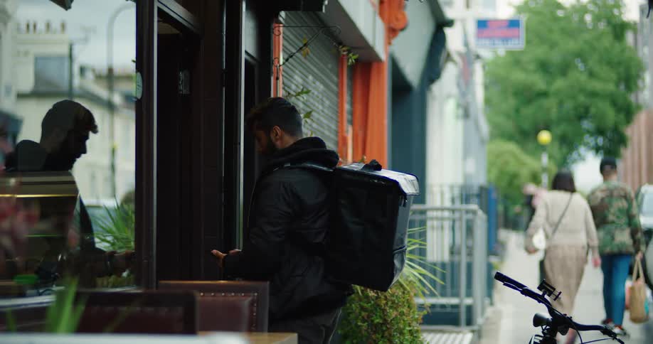 A food delivery driver on his bicycle arrives at a restaurant, checks his phone, and rings the bell for his pickup order