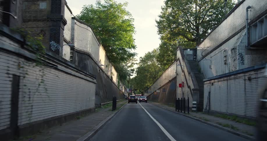 A point of view shot slowly exiting a dark arched tunnel and driving onto a city street with high walls