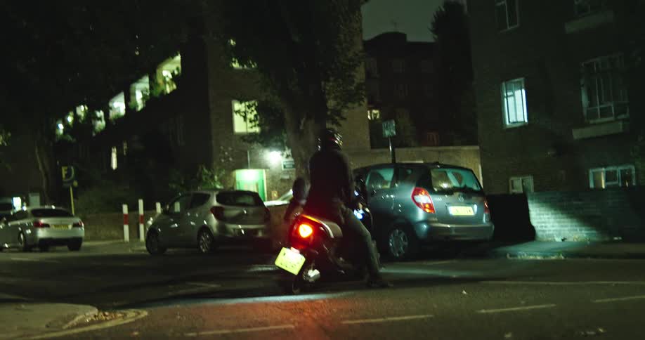 A food delivery cyclist is ambushed and violently robbed of his bicycle by two men on a scooter on a dark city street at night