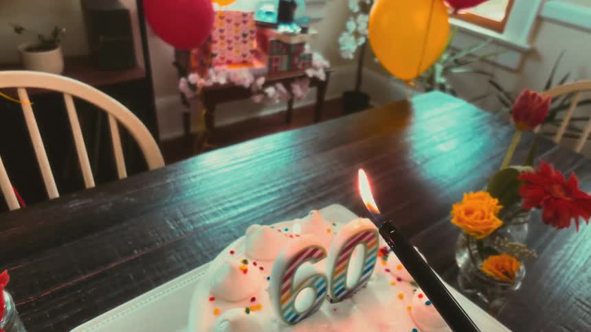 A dreamy, slow-motion shot of lighting the '60' candles on a birthday cake at a festive party