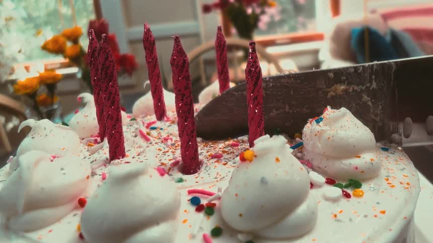 A unique low-angle, slow-motion view shows a knife cutting into a celebratory birthday cake with red candles and colorful sprinkles