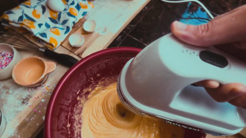 Slow pull-back shot from a first-person perspective shows a baker mixing ingredients with an electric hand mixer
