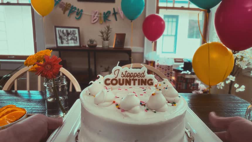 A first-person view of placing a humorous 'I stopped counting' birthday cake on a decorated party table