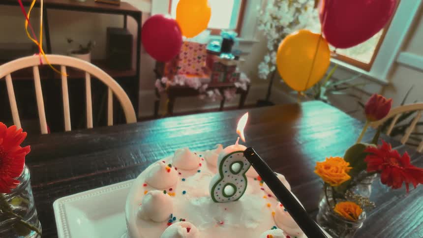 A dreamy, slow-motion POV shot of a number eight birthday candle being lit on a cake in a decorated dining room