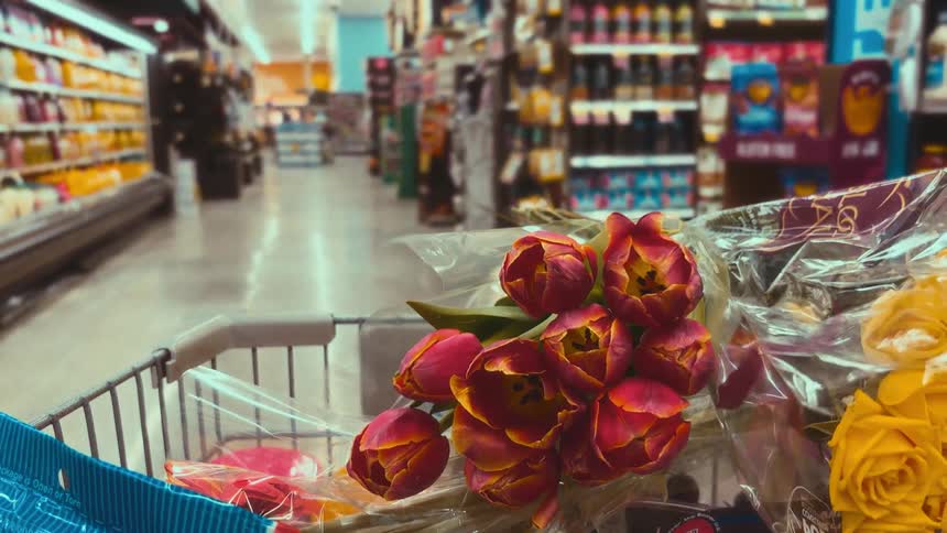 A close-up point-of-view shot of a bouquet of tulips in a shopping cart moving through a grocery store aisle
