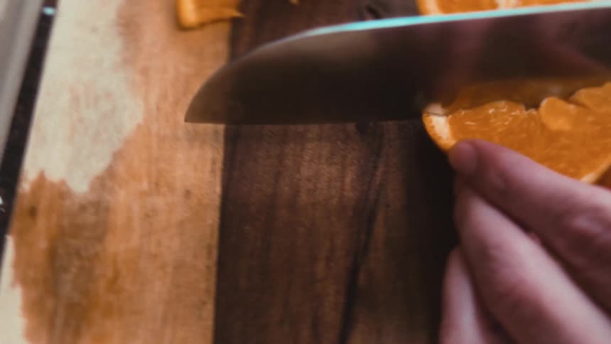 A unique first-person view from a knife as it slices a fresh orange on a wooden cutting board in slow motion