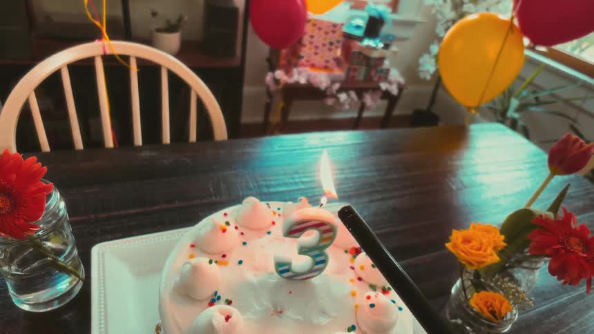 POV slow motion of lighting the number three candle on a birthday cake at a party with balloons, flowers, and fruit