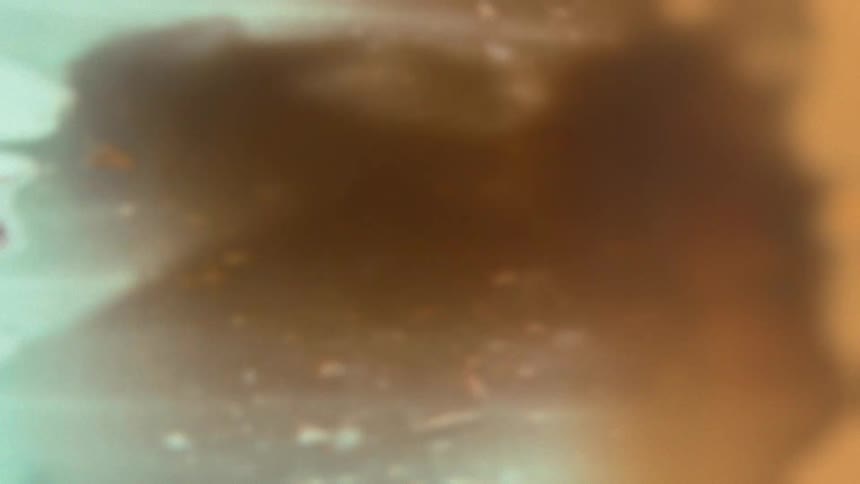 Low-angle POV shot of a smiling man applying thick white plaster directly onto the camera lens with a putty knife