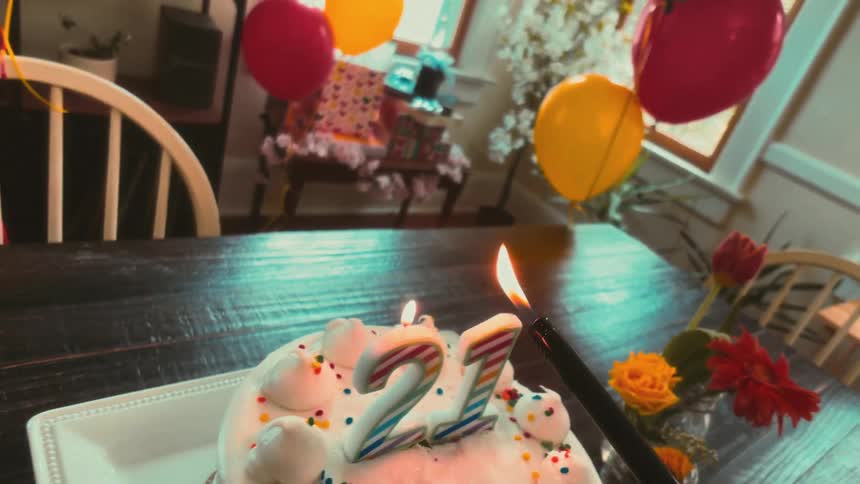 A first-person view of lighting the number 21 candles on a birthday cake at a festive party with balloons and flowers