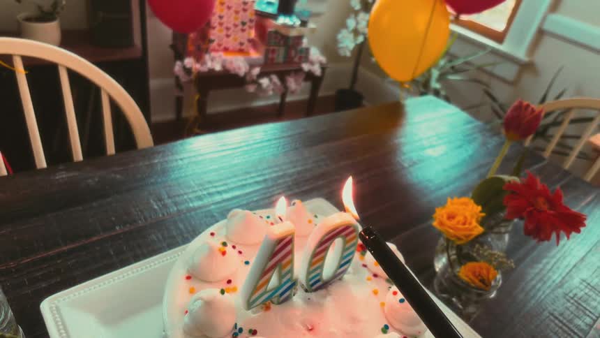 A slow-motion, first-person view of lighting the number '40' candles on a festive birthday cake