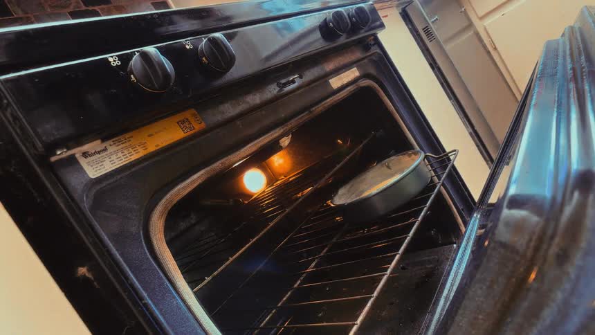 A baker wearing a colorful oven mitt carefully places two cake pans into a hot oven to bake