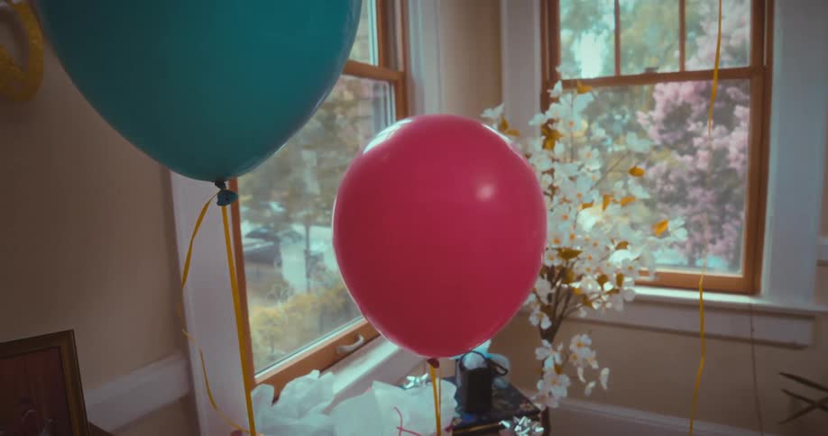 Pink and turquoise balloons float gently in a sunlit room decorated for a party