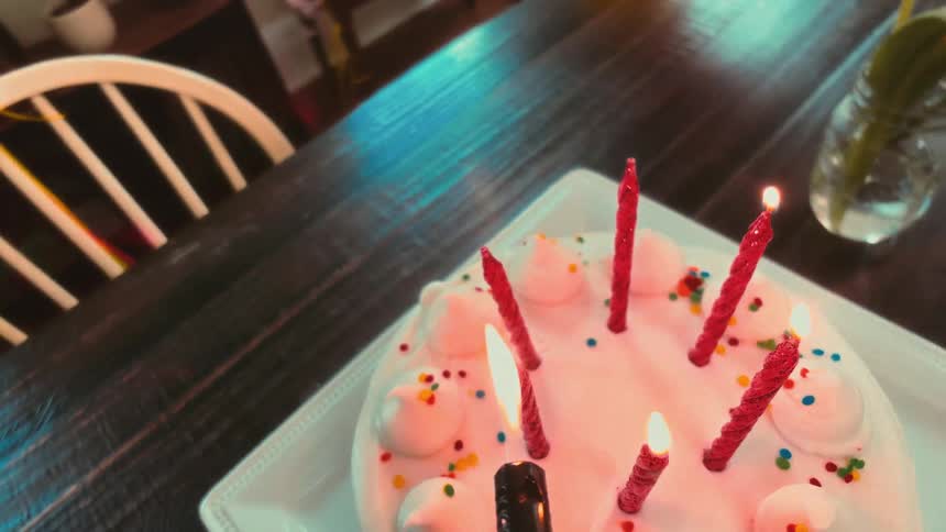 Lighting the red candles on a festive white birthday cake with colorful sprinkles sitting on a wooden table