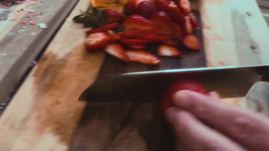 A unique point-of-view shot from a knife blade as it slices fresh strawberries on a wooden cutting board