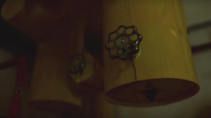 A flashing red emergency light illuminates yellow industrial pipes and valves in a dark, tense boiler room