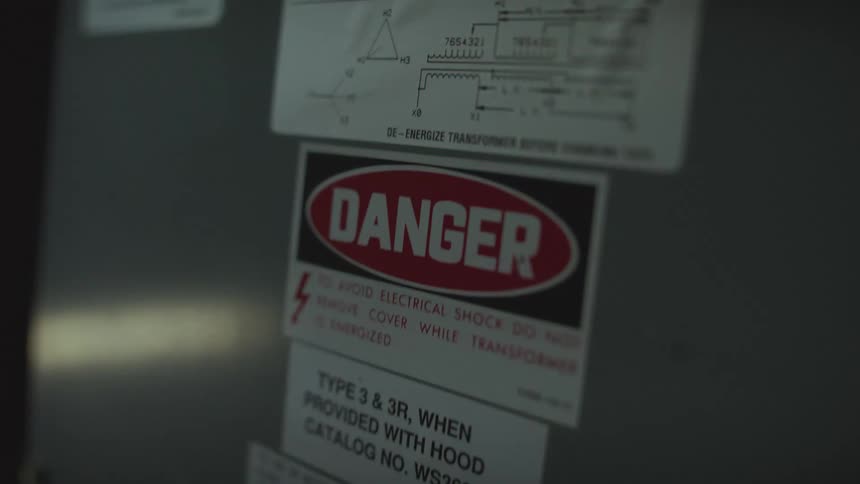 A flashing red warning light illuminates a danger sign on industrial electrical equipment