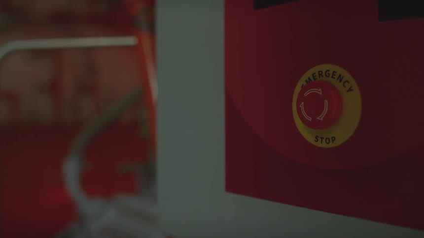A dramatic rack focus shot reveals a large, red emergency stop button on an industrial control panel