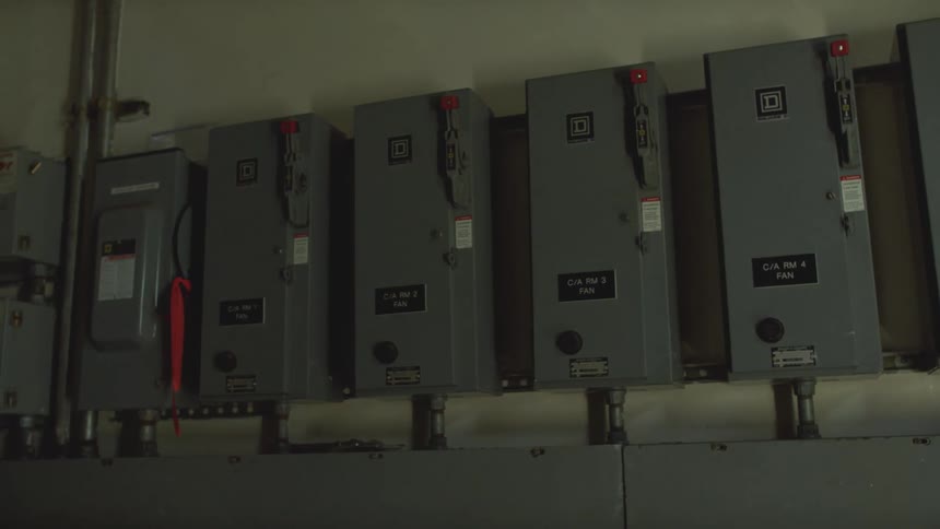 A slow pan across a row of industrial electrical fuse boxes in a dimly lit utility room