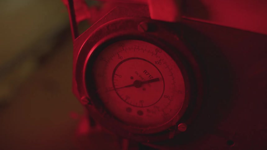 A vintage industrial pressure gauge is illuminated by a pulsing red alarm light in a dark engine room