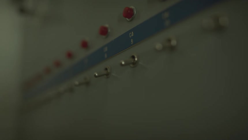 A hand flips a toggle switch on an industrial control panel under a flashing red emergency light