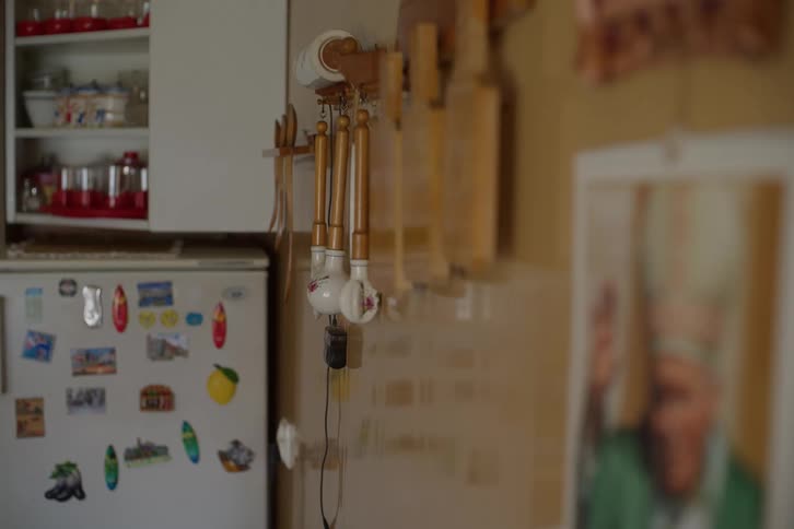 A static shot of a rustic kitchen with hanging wooden utensils and a refrigerator covered in magnets