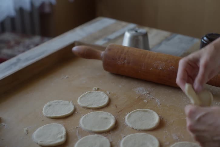 Close-up of a person's hands shaping small pieces of dough for homemade dumplings on a wooden board