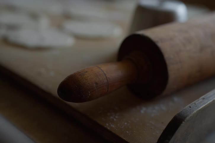 A close-up of a rustic wooden rolling pin resting on a board with fresh dough in the background