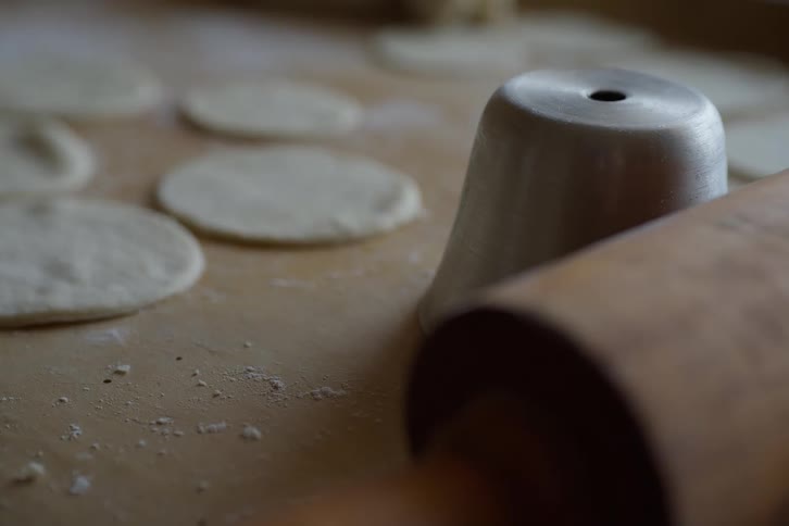 A close-up shot of a wooden rolling pin and metal cutter with fresh dough circles ready for baking on a floured table